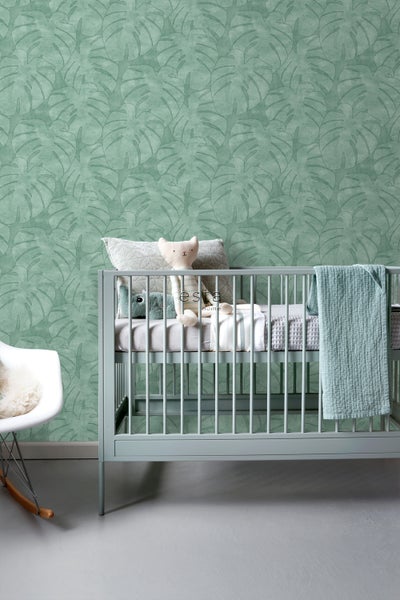 Babyzimmer mit grüner Blättertapete, Kinderbett und Schaukelstuhl