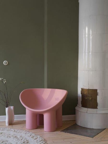 Innenraum mit rosa Sessel, Kaminofen und Vase mit Zweigen