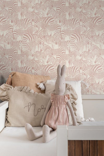 Helle Kinderzimmer-Szene mit Zebra-Tapete, Textilkissen mit Rüschen und Quasten sowie einem Stoffhasen auf einem weißen Bett.