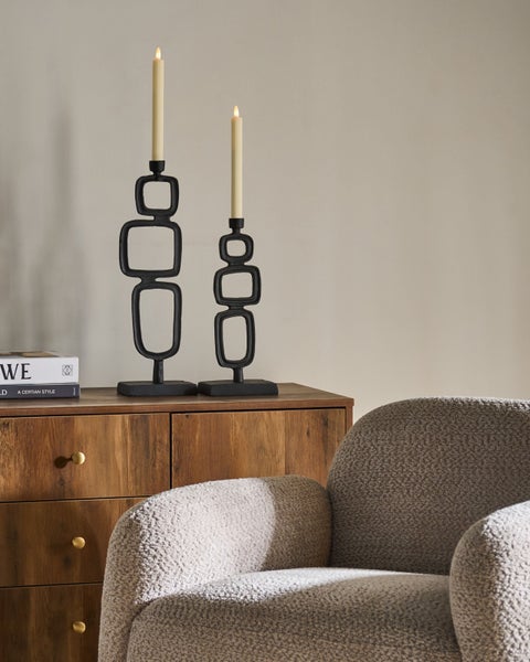 Zwei schwarze Kerzenständer mit Kerzen auf einem Holzschrank neben einem Sessel