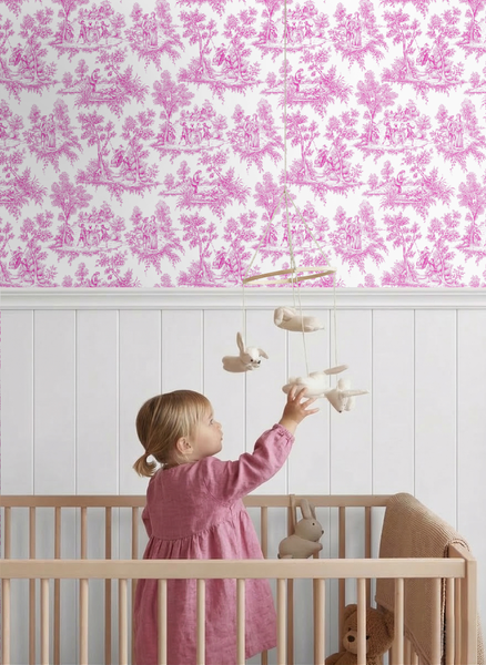Vliestapete mit Toile-de-Jouy-Muster im Kinderzimmer über einer weißen Holzvertäfelung. Ein Kleinkind im Gitterbett greift nach einem Mobile.