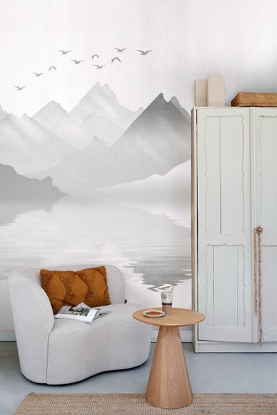 Dekoratives Wohnzimmer mit Sessel, Beistelltisch, Schrank und Fototapete mit Bergmotiv.