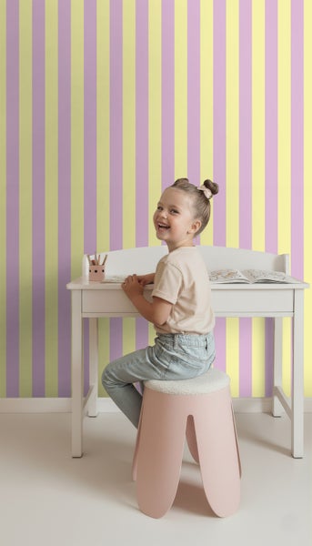 Mädchen sitzt an einem Schreibtisch vor einer Wand mit gestreifter Tapete