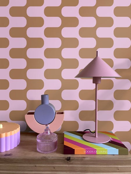 Dekorative Tischleuchte neben Dekoartikeln auf einem Tisch vor einer gemusterten Wand