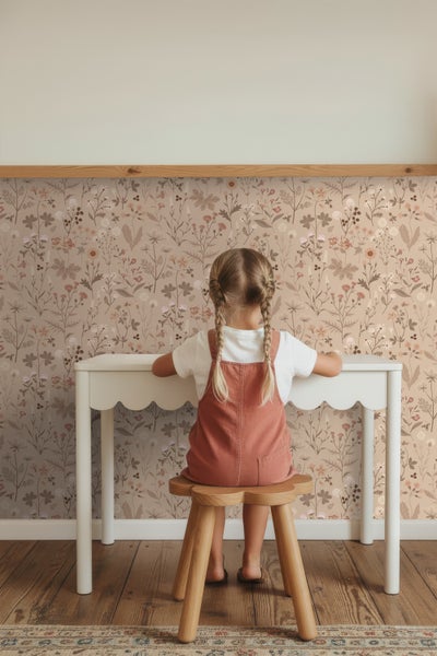 Mädchen sitzt an Schreibtisch vor floraler Tapete
