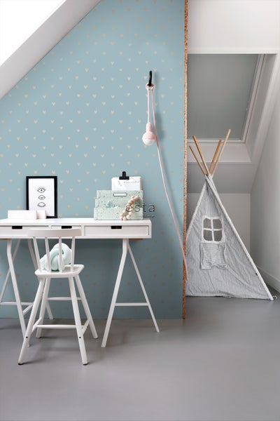 Helles Kinderzimmer mit Schreibtisch, Stuhl, Spielzelt und Wandtapete mit Herzmuster.