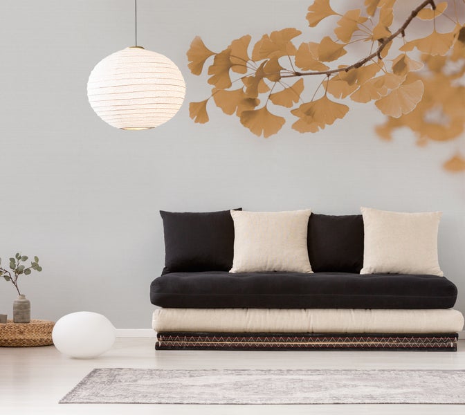 Wohnzimmer mit Ginkgoblatt-Fototapete, einem Futonsofa mit schwarzen und beigen Kissen sowie einer runden Papier-Hängeleuchte.