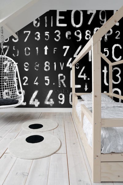 Kinderzimmer mit Holzbettgestell, Hängesessel und runden Teppichen vor einer Wandtapete mit Zahlen und Buchstaben.