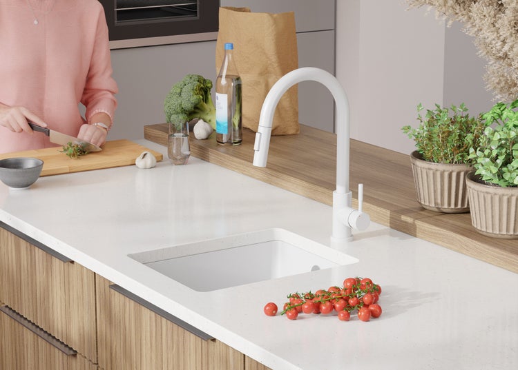 Küchenszene mit Spüle, Armatur, Gemüse und Person beim Kochen