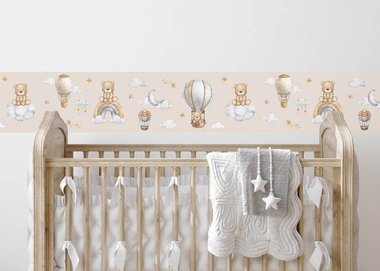 Tapetenbordüre für das Kinderzimmer mit Teddybären, Heißluftballons, Regenbögen und Wolken über einem hölzernen Gitterbett.
