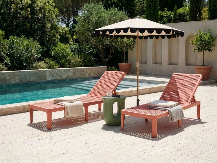 Moderne Poollandschaft mit zwei terrakottafarbenen Sonnenliegen, einem grünen Beistelltisch und einem Sonnenschirm auf einer hellen Steinterrasse.