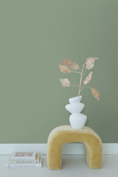 Dekorative Vase mit Kunstpflanze auf einem Hocker vor einer Wand