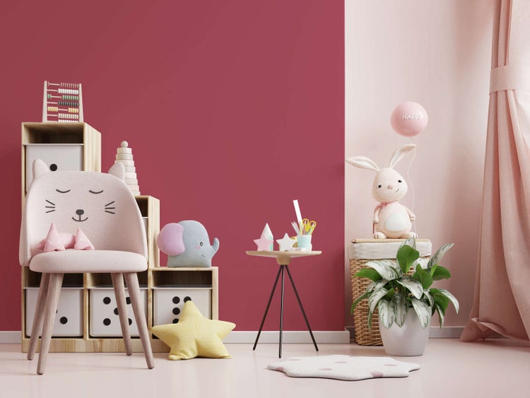 Hell gestaltetes Kinderzimmer mit einer beerenfarbenen Akzentwand, Holzregalen, einem Katzenstuhl sowie verschiedenen Spielzeugen und Pflanzen.