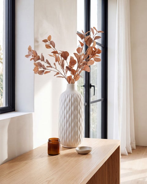 Dekorative Vase aus Keramik mit strukturierter Oberfläche auf einem Holztisch mit Trockenblumen sowie Kerzenglas und kleiner Schale als Dekoration.