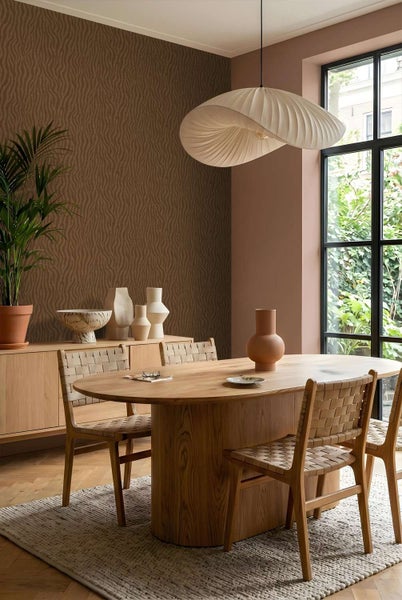 Esszimmer mit gemusterter Tapete, ovalem Holztisch und geflochtenen Holzstühlen in einer modernen, warmen Wohnatmosphäre.