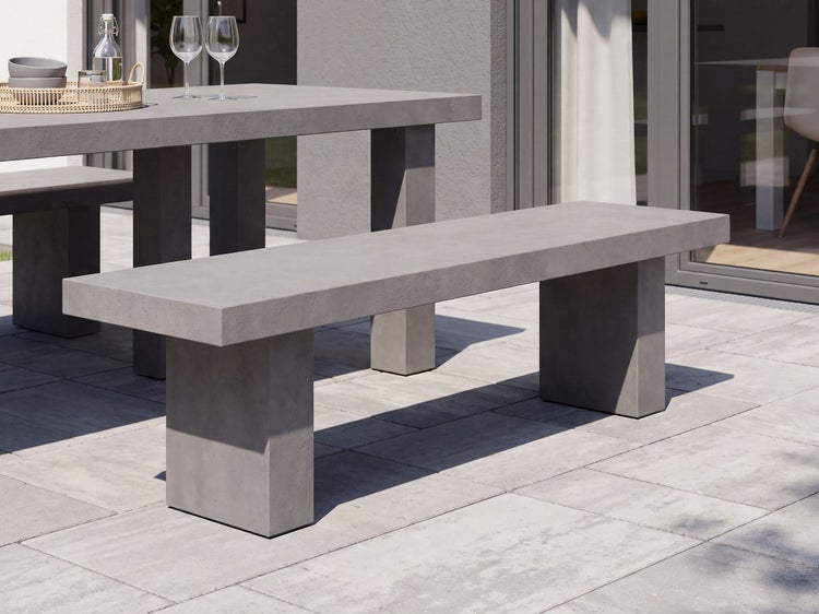 Moderne Gartenbank aus Beton im schlichten Design auf einer Terrasse vor einem Gartentisch.