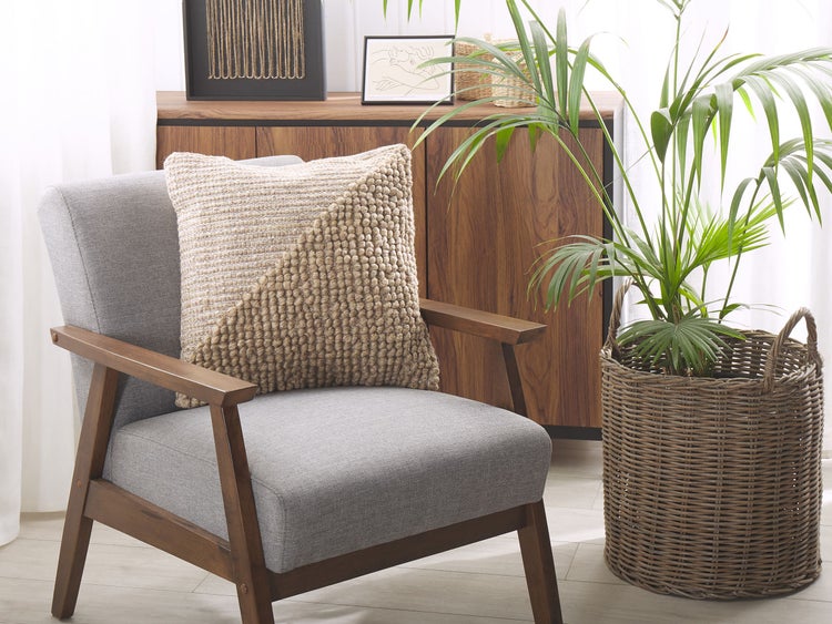 Dekoratives Wohnzimmer mit Sessel, Kissen, Kommode und Zimmerpflanze im Korb