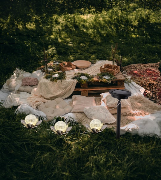 Dekorative Szene im Garten mit Solarleuchten, Kissen und einer Tischdekoration auf einer Europalette.