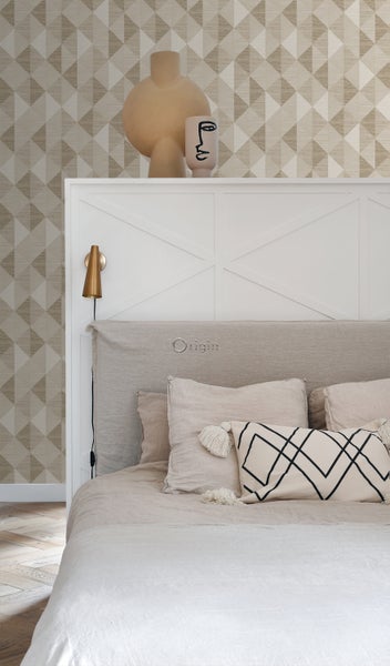 Schlafzimmer mit Bett, Kissen, Wandleuchte und geometrischer Tapete