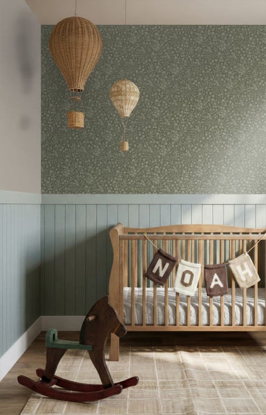 Babyzimmer mit floraler Tapete, hellblauer Wandpaneele, Holz-Gitterbett und Schaukelpferd. Dekorative Heißluftballons aus Korbgeflecht.