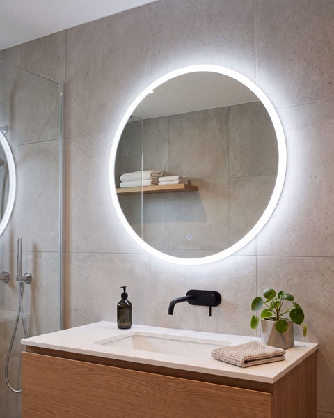 Runder LED Badezimmerspiegel mit Beleuchtung an einer gefliesten Wand über einem Waschbeckenunterschrank mit Unterputzarmatur.