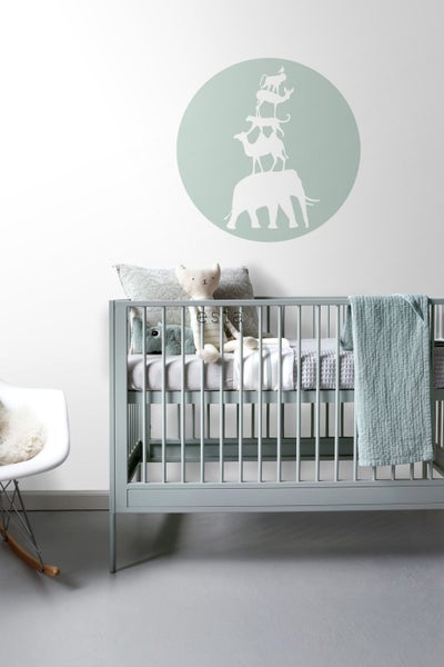 Kinderzimmer mit Babybett, Kissen, Spielzeug und Wandtattoo mit Tiermotiv