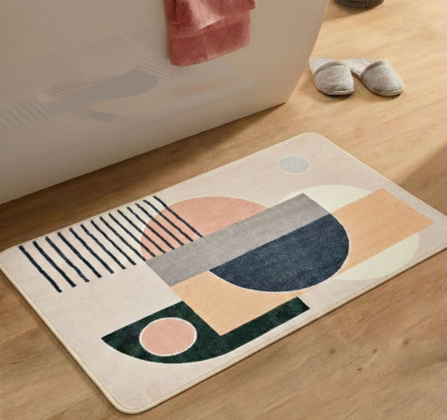 Moderner Badeteppich mit abstraktem geometrischem Muster auf einem Holzboden neben einer Badewanne und Hausschuhen.