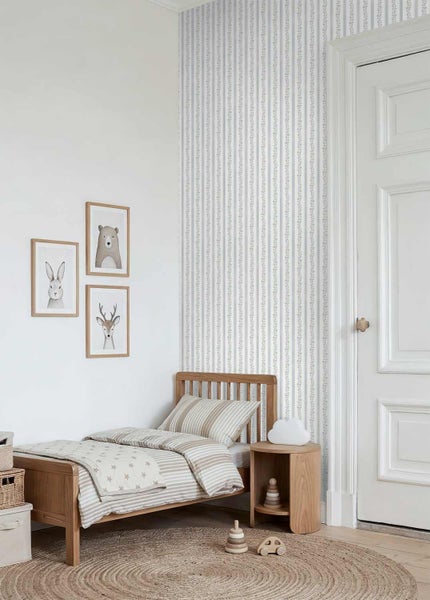 Kinderzimmer mit einem Holzbett, gestreifter Bettwäsche, einer gestreiften Vliestapete und eingerahmten Tierbildern an der Wand.