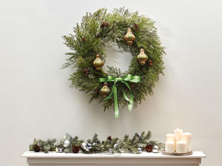 Dekorativer Weihnachtskranz mit Schmuck und Schleife über einem Kaminsims mit Kerzen und Girlande