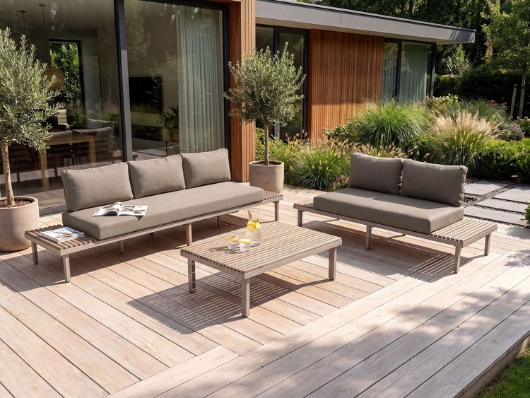 Moderne Loungegarnitur mit Sofas und Couchtisch aus Holz auf einer Holzterrasse vor einem Wohnhaus.