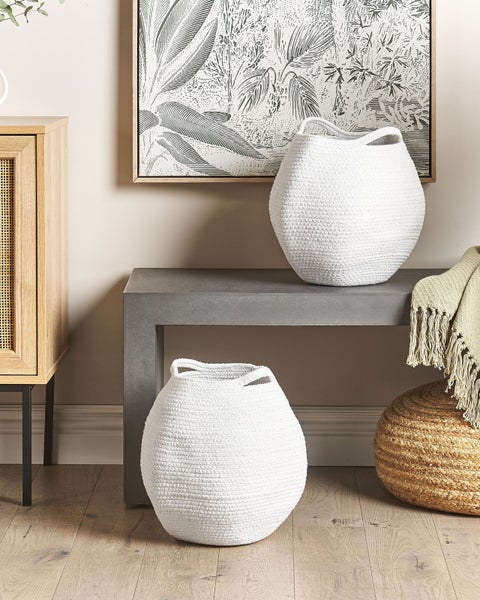 Innenraum mit zwei weißen Seilkörben, einem Holztisch, einem Holzhocker, einem Schrank und einem gerahmten Bild mit Pflanzenmotiven.