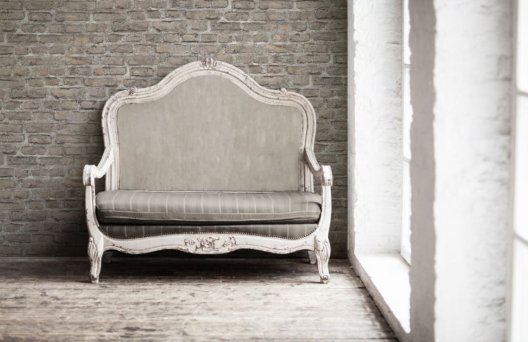 Nahaufnahme einer Wand mit floral gemusterter Tapete und einem vergoldeten Stuhl mit Abdeckung