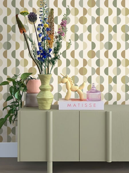 Wohnzimmerszene mit Tapete mit geometrischem Kreismuster, grünem Sideboard, Vase mit Blumen, Matisse Buch und dekorativen Figuren.