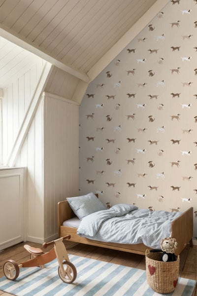 Vliestapete mit Hundemotiven in hellem Kinderzimmer mit Holzbett, gestreifter Bettwäsche und Holzspielzeug unter einer Dachschräge.
