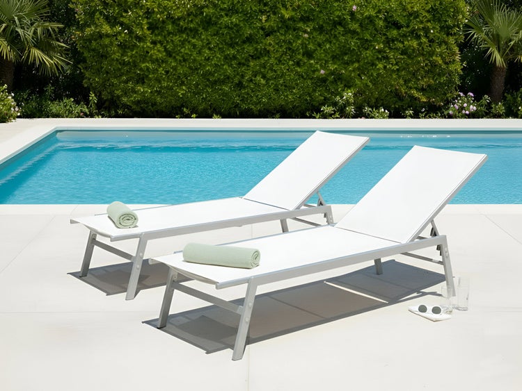 Zwei weiße Sonnenliegen aus Aluminium stehen neben einem Pool.