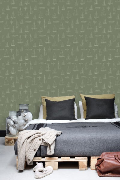 Vliestapete mit Segelschiff-Muster an der Wand hinter einem Palettenbett mit Decke, Kissen und Glasvasen mit Glühbirnen.