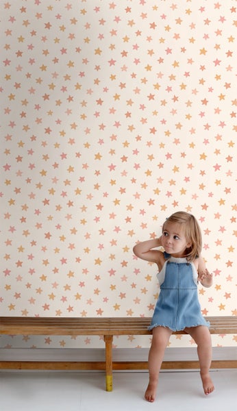 Kinderzimmer mit Sternentapete und einem kleinen Mädchen auf einer Holzbank.