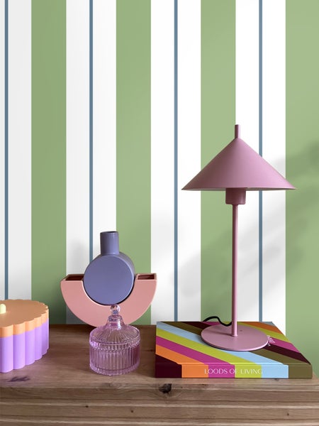 Dekorative Tischszene mit Lampe und Wohnaccessoires auf einem Holztisch vor gestreifter Tapete.