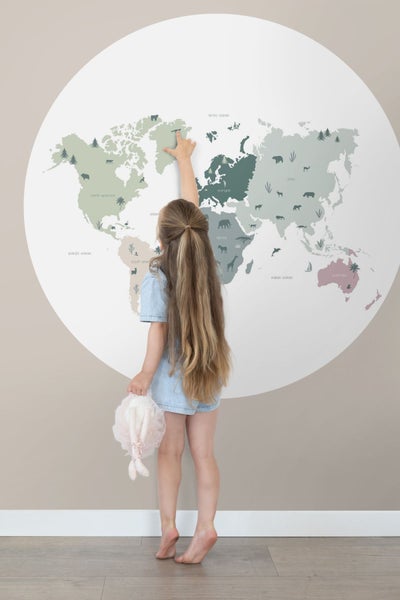 Mädchen zeigt auf eine Weltkarte mit Tierillustrationen an der Wand