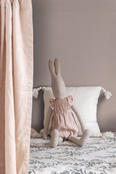 Dekoratives Stofftier Hase im Kinderzimmer auf Kissen und floral gemusterter Decke