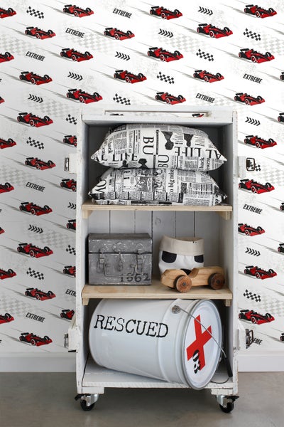 Regal mit Kissen, Metallkiste, Stoffbeutel, Holzspielzeugauto und Metalleimer vor einer Tapete mit Rennwagenmuster