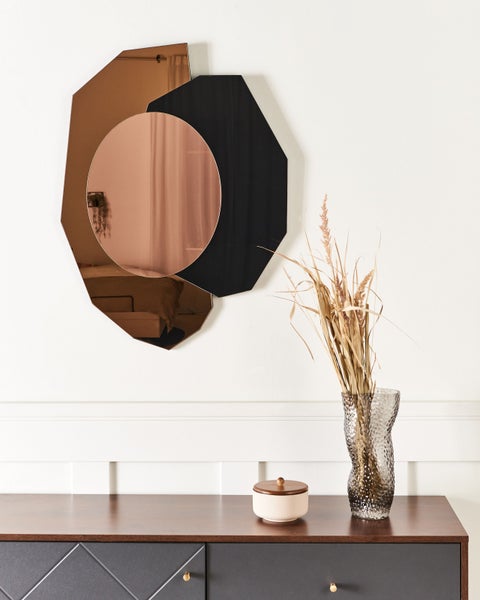 Dekorativer Spiegel mit geometrischen Formen an einer Wand über einem Schrank.