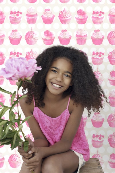Lachendes junges Mädchen mit Blume vor Tapete mit Cupcake-Muster