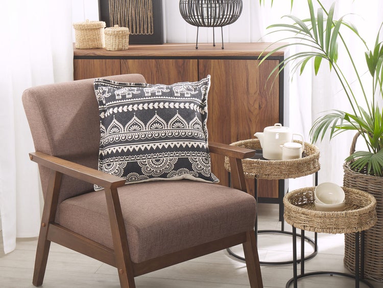 Wohnzimmer-Szene mit Sessel, Kissen mit Elefantenmuster, Beistelltischen und Dekoration