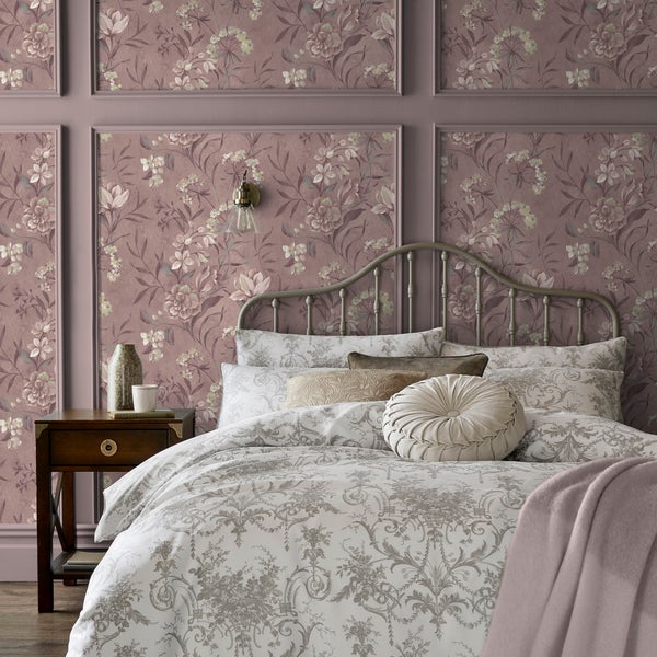 Schlafzimmer mit floraler Tapete in dekorativen Wandleisten, Bett mit gemusterter Bettwäsche und einem Nachttisch aus Holz.