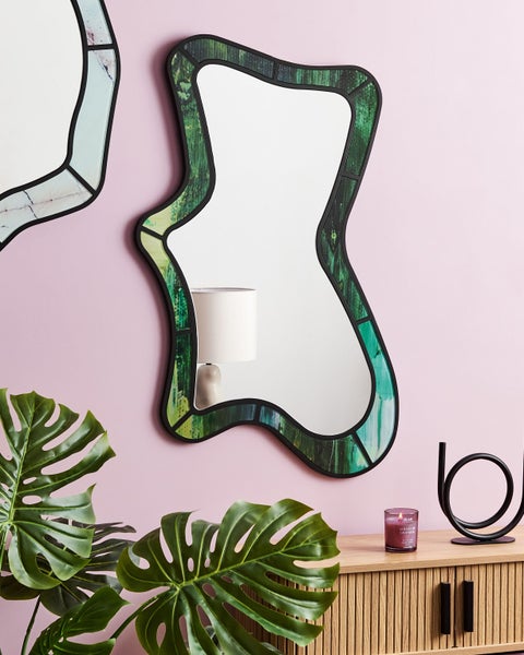 Dekoratives Interieur mit einem Spiegel mit unregelmäßiger Form und grünem Muster an einer Wand.