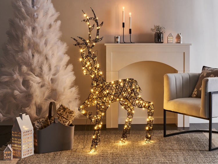 Weihnachtliche Dekoration mit beleuchtetem Rentier, künstlichem Baum und Kamin