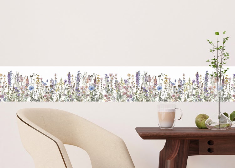 Modernes Wohnzimmer mit floraler Tapetenborte an einer strukturierten Wand, Holzsessel mit Decke, Beistelltisch und buntem Teppich.