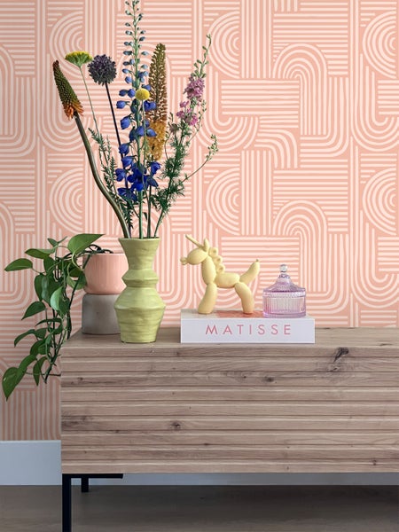 Dekoratives Interieur mit Blumen, Vase und gemusterter Tapete auf Kommode