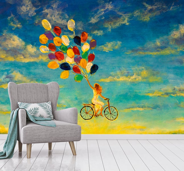 Fototapete mit gemaltem Motiv einer Person auf einem Fahrrad mit Luftballons, Polstersessel und Holzboden in hellem Zimmer.